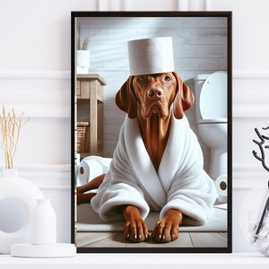 May include: A brown and white dog wearing a white bathrobe and a toilet paper roll hat. The dog is sitting on a white bathroom floor with a toilet in the background.