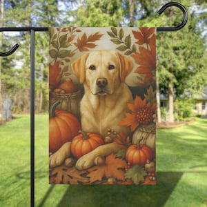 May include: A decorative garden flag featuring a golden Labrador Retriever surrounded by pumpkins, fall leaves, and gourds. The artwork has a warm, autumnal color palette, perfect for fall decor. The flag is displayed on a black metal stand.