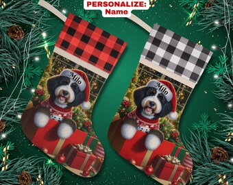 May include: Personalized Christmas stocking featuring a black and white dog with a red Santa hat, peeking out of a red gift box. The stocking has a red and black buffalo plaid cuff and the dog's name, "Milo", is embroidered on the stocking.