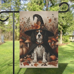 May include: A garden flag featuring a Cavalier King Charles Spaniel dressed as a witch. The dog wears a black witch hat and cape, surrounded by pumpkins, mushrooms, and autumn leaves. The flag is displayed on a black metal stand.