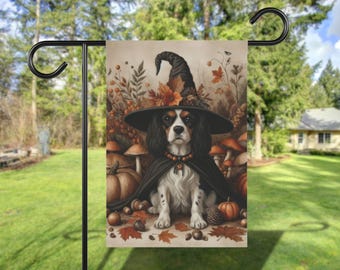 May include: A garden flag featuring a Cavalier King Charles Spaniel dressed as a witch. The dog wears a black witch hat and cape, surrounded by pumpkins, mushrooms, and autumn leaves. The flag is displayed on a black metal stand.