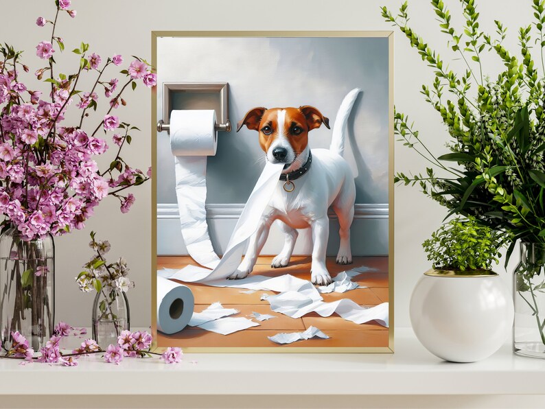 Puede incluir: Una pintura enmarcada de un perro blanco y marr&oacute;n con un collar negro, de pie en un ba&ntilde;o con un rollo de papel higi&eacute;nico en el suelo. El perro ha tirado del papel higi&eacute;nico del rollo y est&aacute; de pie sobre el papel rasgado.