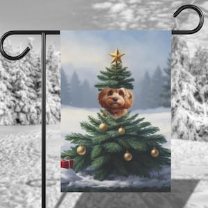 May include: A brown and white dog peeking out from behind a green Christmas tree decorated with gold ornaments. The tree is set against a snowy background with a blue sky.
