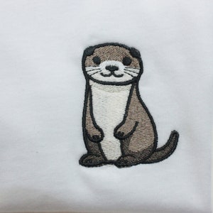 Op de afbeelding: Geborduurde afbeelding van een bruine en witte otter op een wit T-shirt.