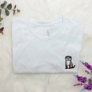 Op de afbeelding: Wit T-shirt met een geborduurd otterontwerp. De otter is bruin en zit rechtop.