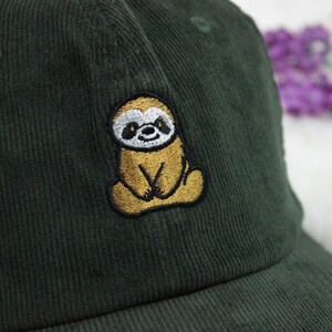 Op de afbeelding: Een donkergroene corduroy baseballpet met een geborduurd geel luiaard op de voorkant.