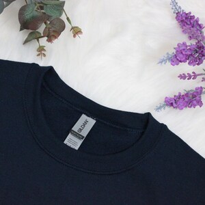 Op de afbeelding: Een donkerblauw sweatshirt met een Gildan-merketiket bevestigd aan de hals.