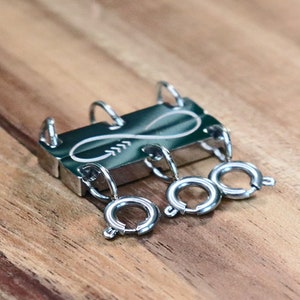 May include: A silver metal key chain with four rings and an infinity symbol design. The key chain is on a wooden surface.