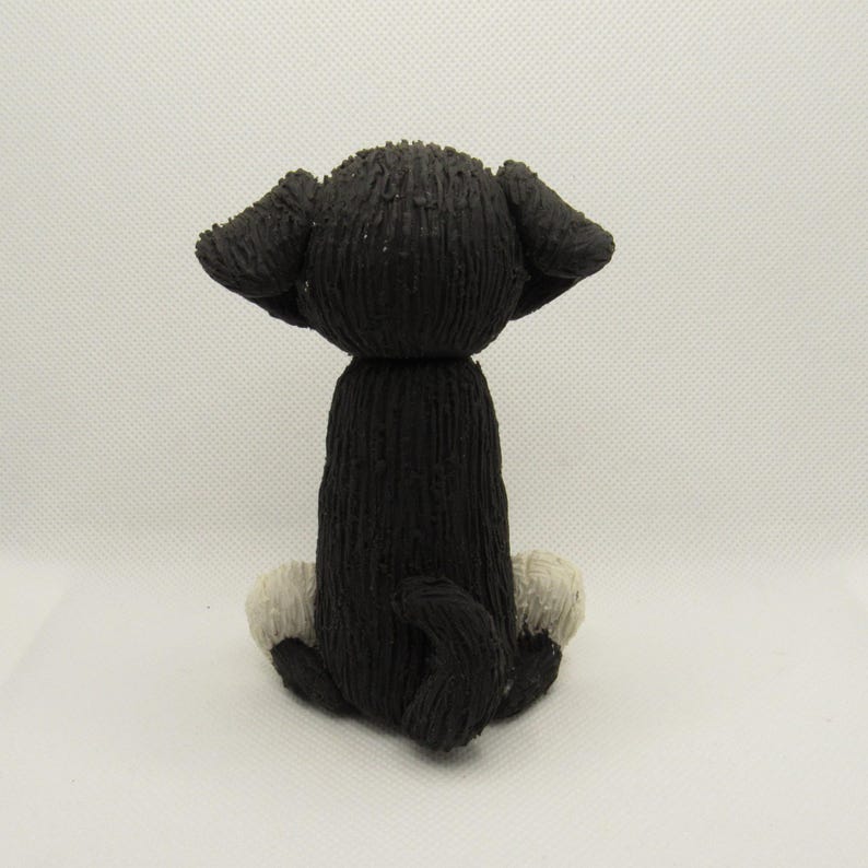 May include: Black and white ceramic dog figurine sitting on its hind legs with its tail curled around its legs. The dog has white paws and a black body.