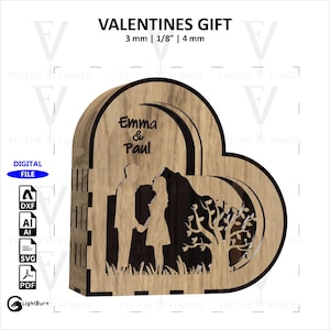 Pode incluir: Uma caixa de madeira em forma de coração com um design recortado de um casal em pé em frente a uma árvore. A caixa é personalizada com os nomes "Emma & Paul" e tem uma espessura de 3 mm, 1/8 de polegada ou 4 mm.