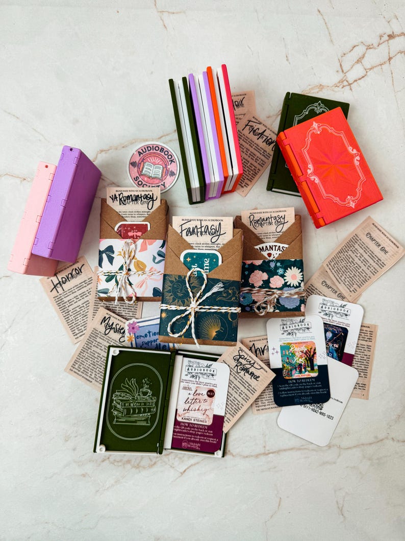 K&ouml;nnte beinhalten: Eine Auswahl an Miniaturb&uuml;chern und Artikeln zum Thema B&uuml;cher. Es gibt mehrere kleine, farbenfrohe B&uuml;cher, zusammen mit Papier-Ephemera und dekorativen Verpackungen zum Thema B&uuml;cher. Die Artikel sind auf einer hellen Oberfl&auml;che angeordnet.