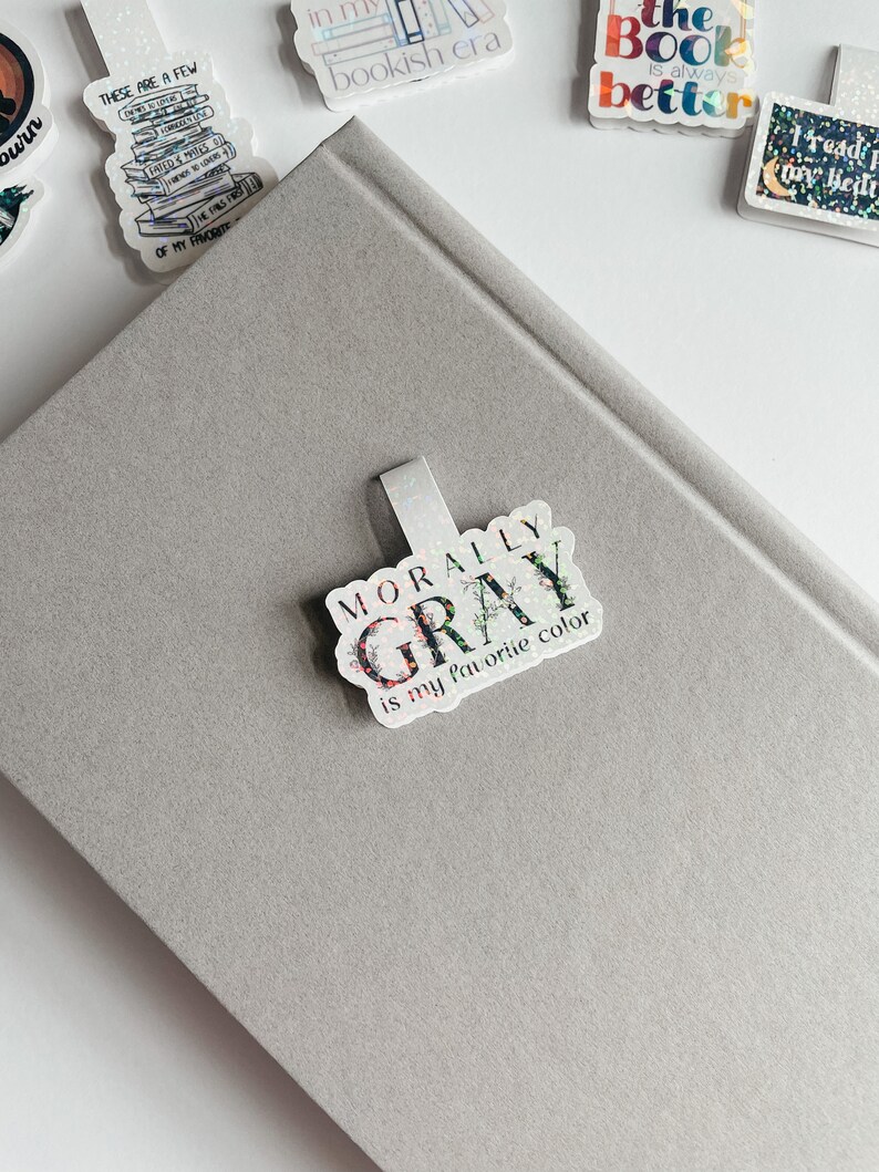 May include: A silver glitter bookmark with the text "Morally Gray is my favorite color" in black and white lettering.
