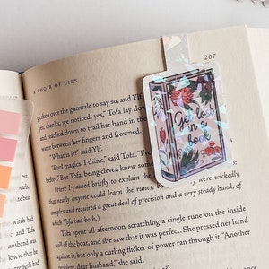 May include: A book bookmark with a floral design and the text "Get lost in a book". The bookmark is made of clear plastic with a holographic finish.