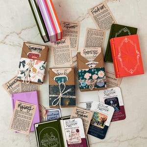 K&ouml;nnte beinhalten: Eine Auswahl an bunten Miniaturb&uuml;chern und thematischen Karten. Die B&uuml;cher sind in verschiedenen Farben gehalten, darunter Gr&uuml;n, Orange und Lila. Die Karten zeigen Texte wie "Romantasy", "Mystery" und "Spicy Romance".