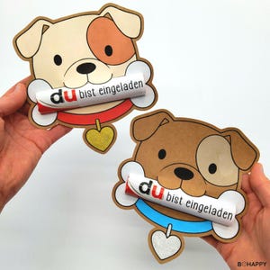 May include: Two dog-shaped greeting cards. One is tan with a brown ear and eye patch, the other is brown with a tan ear and eye patch. Each holds a bone-shaped scroll with German text. Both have a heart-shaped tag.