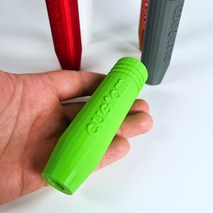 Peut inclure: Un objet cylindrique vert vif avec le mot "custom" en relief sur le côté. L'objet est fait d'un matériau texturé et semble être un stylo ou un petit outil.