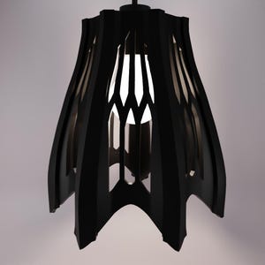 May include: Black pendant light with a geometric design. The light has vertical cutouts and a pointed base. The interior is white, and the exterior is black. The light is suspended from a black cord.