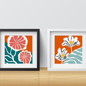 May include: Two framed prints with abstract floral designs. The print on the left features pink flowers on a teal and orange background. The print on the right features white flowers with black outlines on a blue and orange background.
