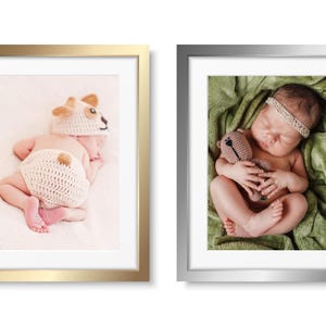 May include: Two framed photographs of a newborn baby. The photo on the left shows the baby wearing a crocheted animal hat and nappy. The photo on the right shows the baby sleeping on a green blanket, holding a crocheted teddy bear.