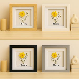 May include: Four square framed floral art pieces. Each frame is a different colour: yellow, white, black, and grey. Each frame contains a yellow flower with the word "Bloom" printed below it.