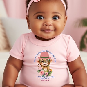 May include: A pink baby onesie with a cartoon monkey wearing a hat and glasses. The onesie has the text "This is the day that the Lord has made" and "I will rejoice and be glad in it. Psalm 118:24".