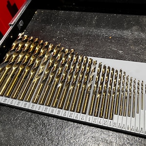 Peut inclure: Un ensemble de mèches dorées organisées dans un porte-mèches en plastique gris. Les mèches sont disposées par ordre de taille, les plus petites à droite et les plus grandes à gauche. Le porte-mèches est marqué pour indiquer la taille de chaque mèche.