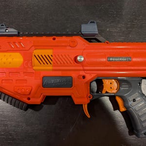 May include: Orange and gray Adventure Force Spectrum toy blaster. The toy gun has a black handle, orange trigger, and orange and yellow accents. The text "SPECTRUM" and "ADVENTURE FORCE" are visible on the blaster.