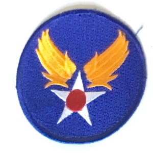 May include: A circular patch with a blue background features a white star with a red center and two yellow wings. The patch is likely an emblem or insignia, possibly for a military or aviation organization.