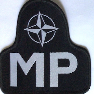 May include: Black patch with a white NATO star emblem and the letters "MP" in white. The patch has a rounded top and a rectangular base. The emblem is a four-pointed star inside a circle.