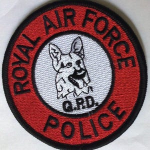 May include: Embroidered patch with a red border and black trim. The text "ROYAL AIR FORCE POLICE" is in black, encircling a white circle with a black and white dog illustration and the letters "G.R.D."