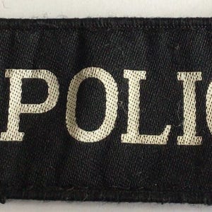 May include: A rectangular black fabric patch featuring the word POLICE embroidered in silver thread. To the left, a circular emblem displays a red rose at the center, surrounded by a blue border with the text LANCASHIRE CONSTABULARY, topped by a crown.