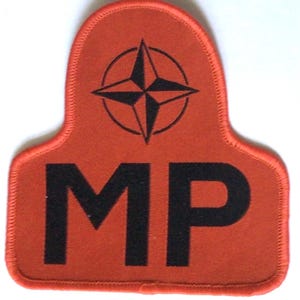 May include: A red patch with black text and a black compass rose design. The letters "MP" are prominently displayed in bold, black font. The patch has a stitched border.