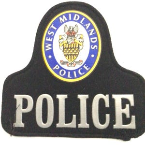 Peut inclure: Écusson d'épaule de police noir avec l'inscription "POLICE" en lettres argentées. L'écusson comporte un emblème circulaire avec "WEST MIDLANDS POLICE" en bleu et un blason au centre.