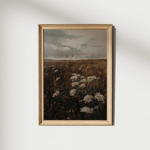 May include: A framed print of a field of wildflowers with a cloudy sky in the background. The flowers are white and the field is a muted brown color.