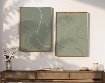 May include: Two framed abstract art prints. Each print features a sage green background with flowing, curved lines in lighter shades of green and white. The frames are a warm, natural wood tone, adding a touch of elegance to the minimalist design.