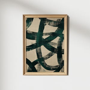 May include: Abstract art print in a wooden frame. The artwork features dark teal brushstrokes on a beige background. The brushstrokes are layered and create a sense of movement. The frame is a light wood color.