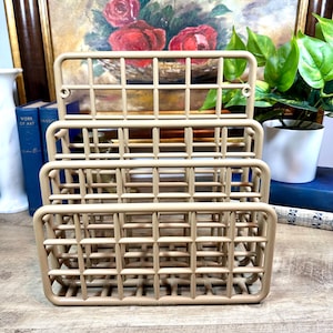 May include: A beige metal magazine rack with three tiers. The rack is made of a wire mesh design and has a rectangular shape.