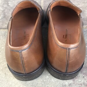May include: A pair of brown leather loafers with black soles. The loafers have a simple design and are made of high-quality leather.