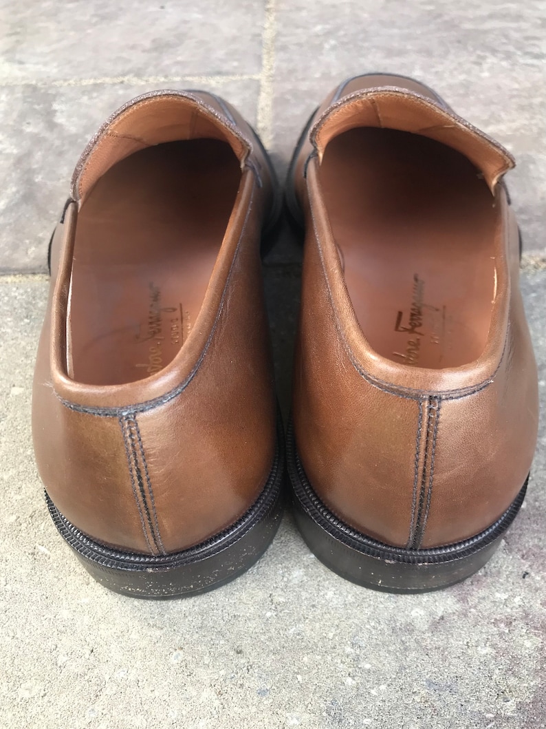 May include: A pair of brown leather loafers with black soles. The loafers have a simple design and are made of high-quality leather.