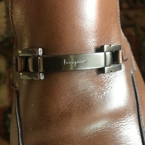 May include: Close-up of a brown leather shoe with a silver buckle and the word "Ferragamo" engraved on it.