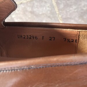 May include: Close-up of the inside of a brown leather shoe with the size and style number printed on the insole. The text reads "UH23296 F 27 7 1/2 E".