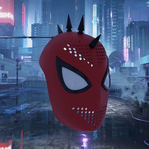 Op de afbeelding: Een rood en zwart Spider-Man-masker met een zwart gaasontwerp en spikes aan de bovenkant. Het masker zweeft voor een futuristische stadsachtergrond.