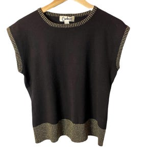 Può includere: Maglia nera senza maniche con bordino dorato intorno al collo e all'orlo. La maglia ha l'etichetta "Carducci" sul davanti.