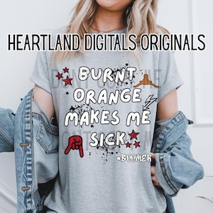 May include: A light gray t-shirt with the text "BURNT ORANGE MAKES ME SICK" in white, with red star and hand graphics. The shirt also has the text "#BOOMER". The words "HEARTLAND DIGITALS ORIGINALS" are at the top.
