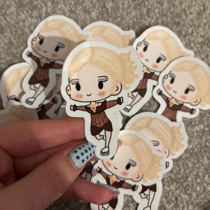 Puede incluir: Una colección de pegatinas con un personaje de dibujos animados con pelo rubio y un atuendo marrón. El personaje está en una pose dinámica con los brazos extendidos. Las pegatinas tienen un borde blanco.
