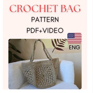 Könnte beinhalten: Häkeltaschen-Anleitung in englischer Sprache, PDF- und Videoformat. Die Tasche ist beige und hat eine quadratische Form mit einem runden Design in der Mitte. Die Tasche liegt auf einer weißen, flauschigen Oberfläche.