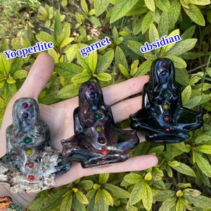 Op de afbeelding: Drie kleine, handgesneden beeldjes van een vrouw in een zittende meditatiehouding. Elk beeldje is gemaakt van een ander type steen: yooperliet, granaat en obsidiaan. Elk beeldje heeft zeven kleine stenen die de zeven chakra's voorstellen.