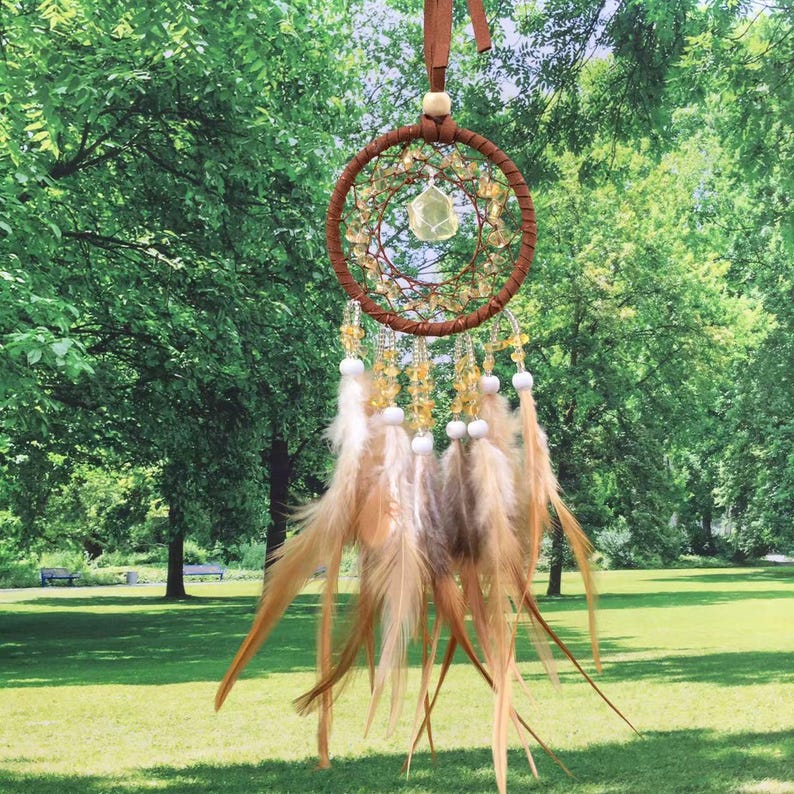 May include: A brown dream catcher with a yellow crystal in the center and brown feathers hanging from the bottom.