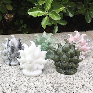 May include: A collection of carved fox figurines in various colors, including white, green, pink, and gray. Each fox has multiple tails and is sitting upright. The figurines are displayed on a speckled surface.