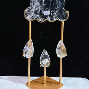 May include: A gold-coloured metal stand featuring a cloud-shaped clear crystal at the top and three teardrop-shaped clear crystals suspended below. The cloud and the centre teardrop each have a small white sticker with the number 13 attached.